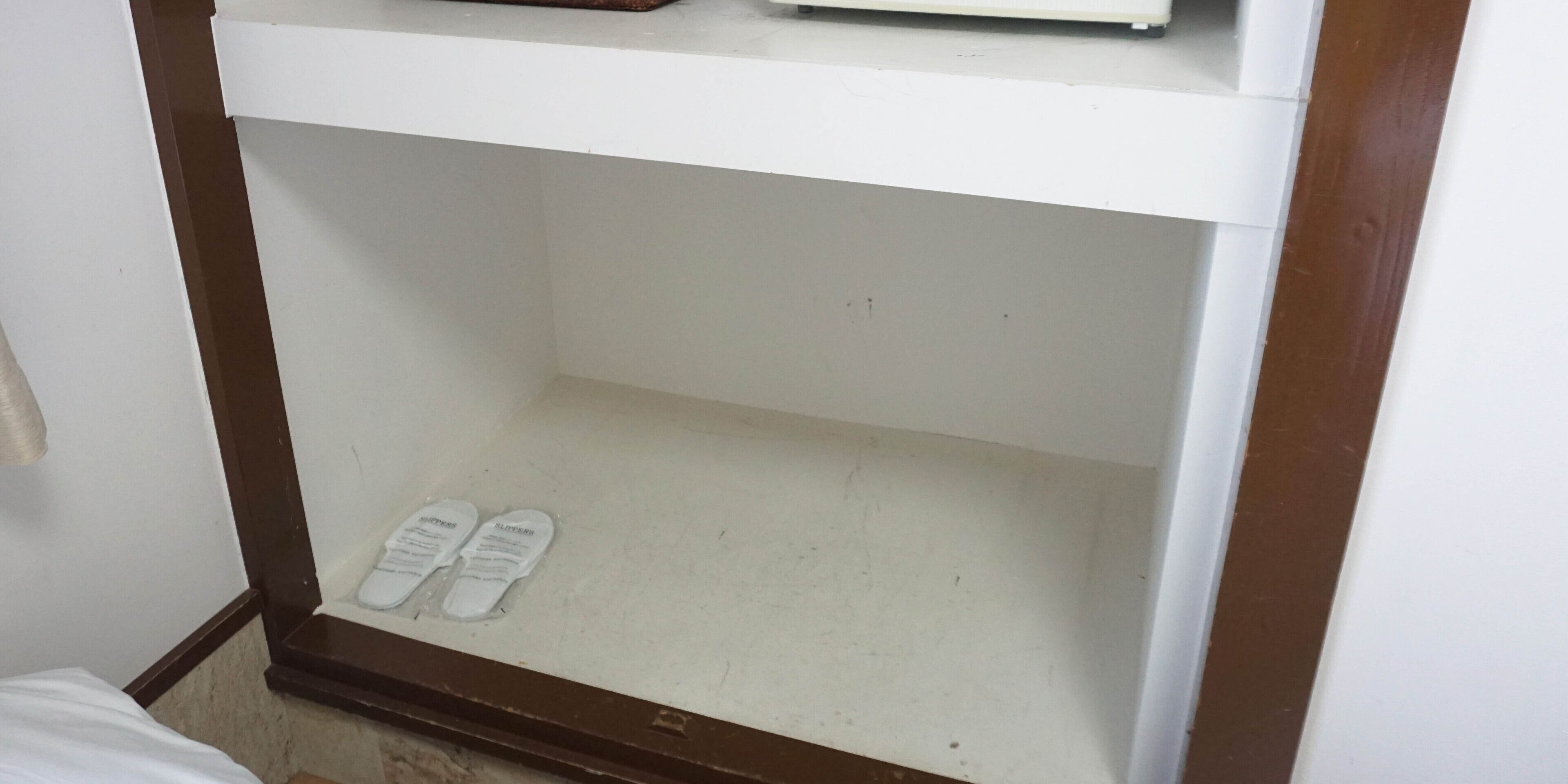 A white shelf with a pair of white slippers on it.