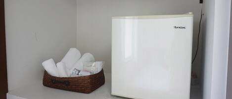 A white refrigerator with a brand name, a wicker basket with towels, and a power cord plugged in.