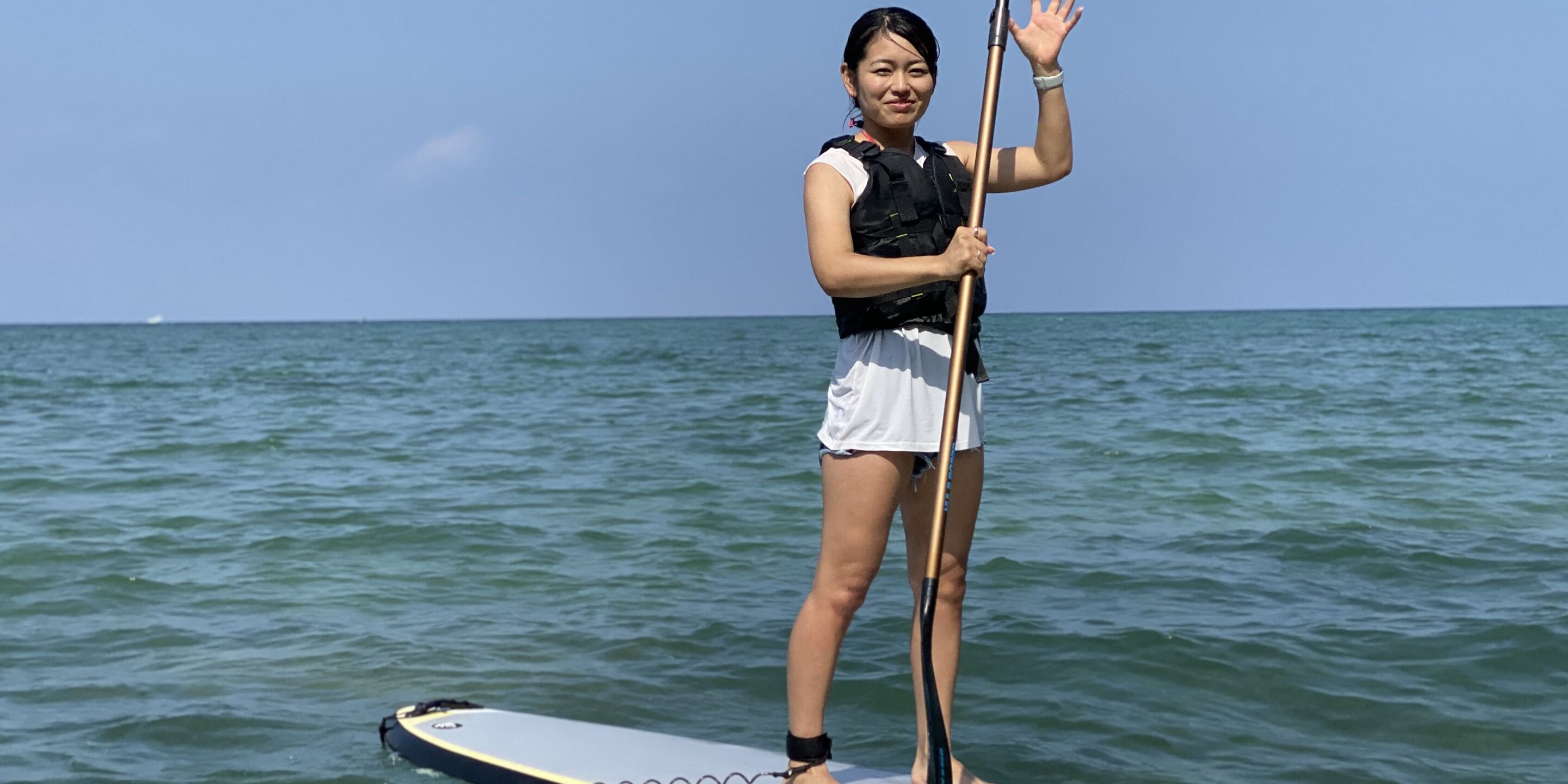 A person standing on a paddleboard in the water, wearing a life jacket and holding a paddle.