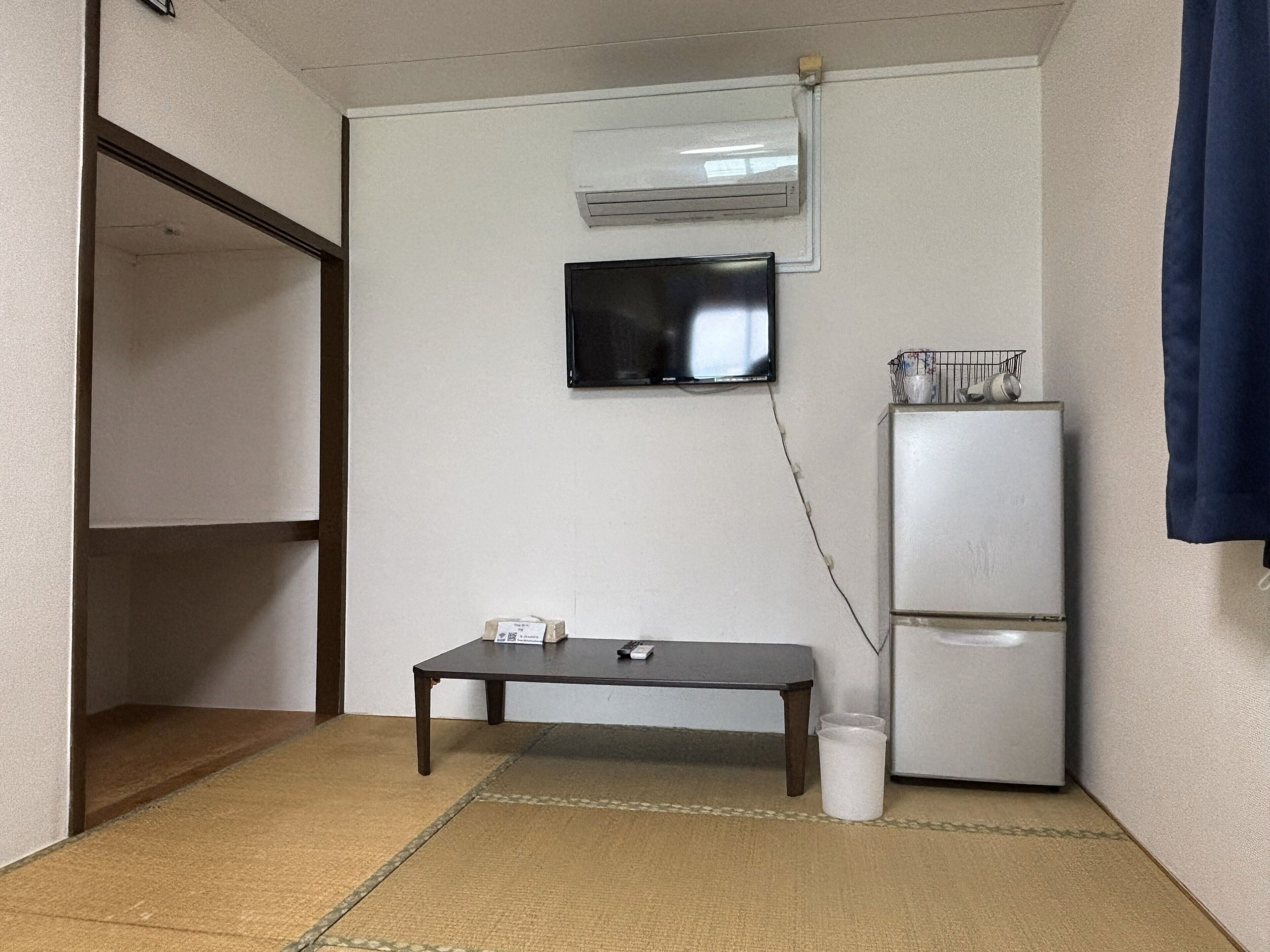 A small, compact room with a single table, a refrigerator, and a mounted television.