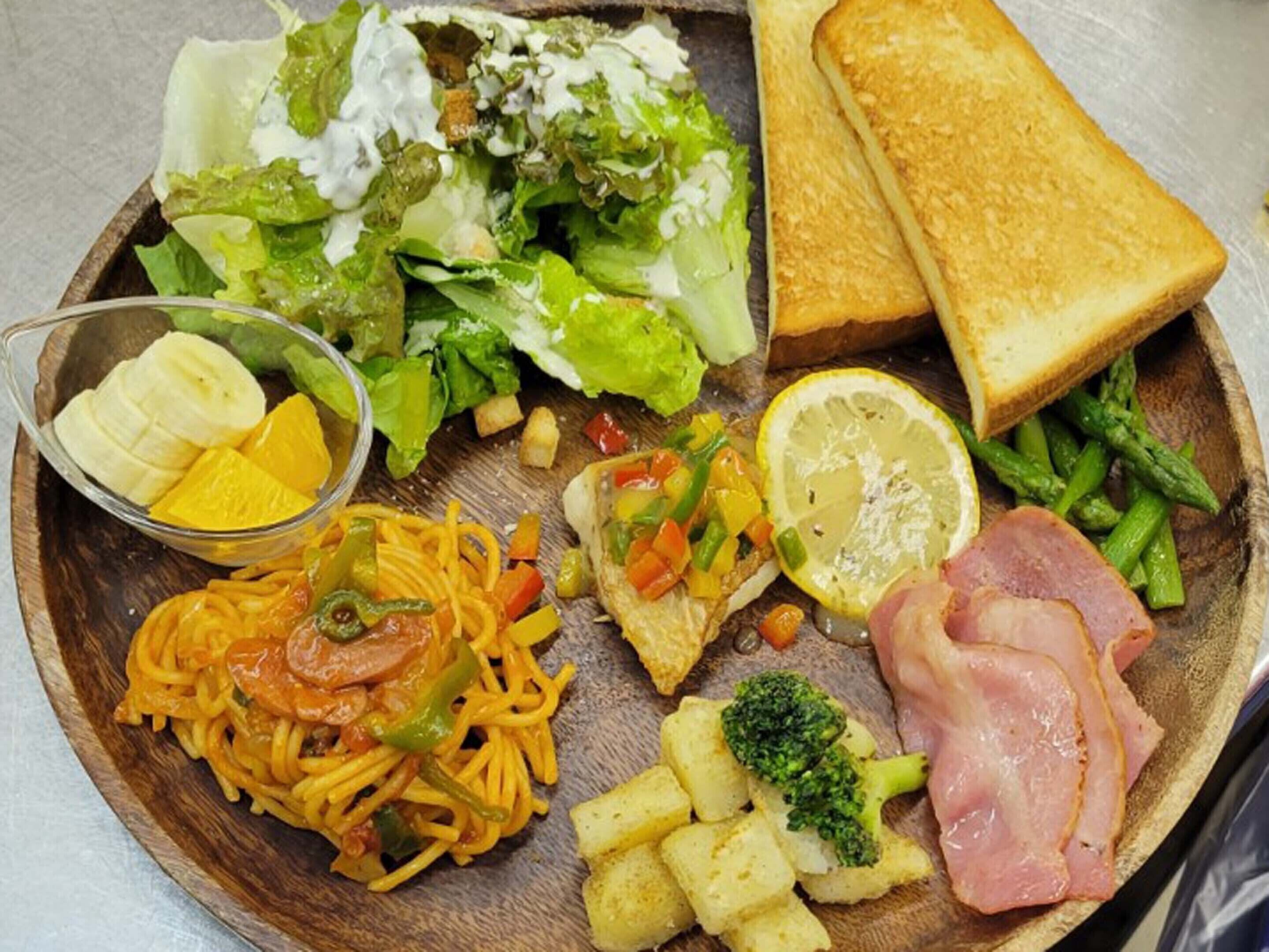 Ett träbricka med ett urval av matvaror, inklusive pasta, grönsaker, bröd och en sallad.