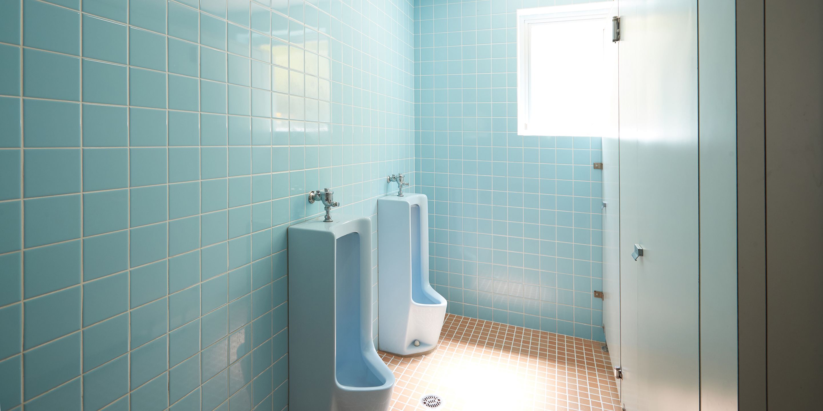 A bathroom with blue tiled walls and floor, two urinals, and a white door.