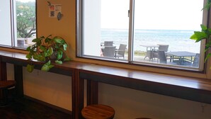 A room with a large window overlooking the ocean, a wooden bar area, and a seating area with chairs and tables. - Hotel Oceans Nakijin (Nakijin)