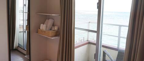 Un balcón con vista al mar, una silla de mimbre y un estante con toallas.