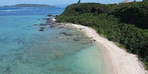 A coastal beach with clear turquoise waters, a sandy shore, and lush greenery on the hillside.