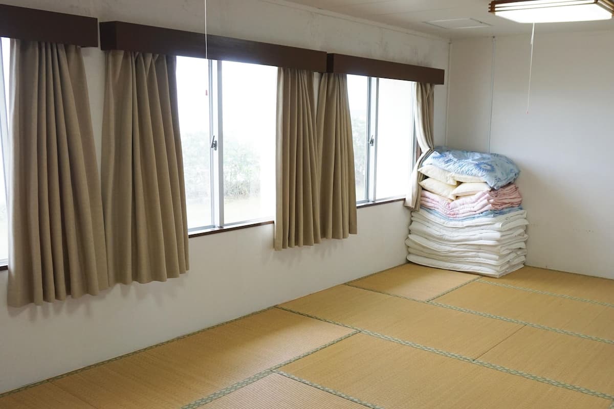 A room with tatami mat flooring, a stack of pillows, and a small table with a tissue box.