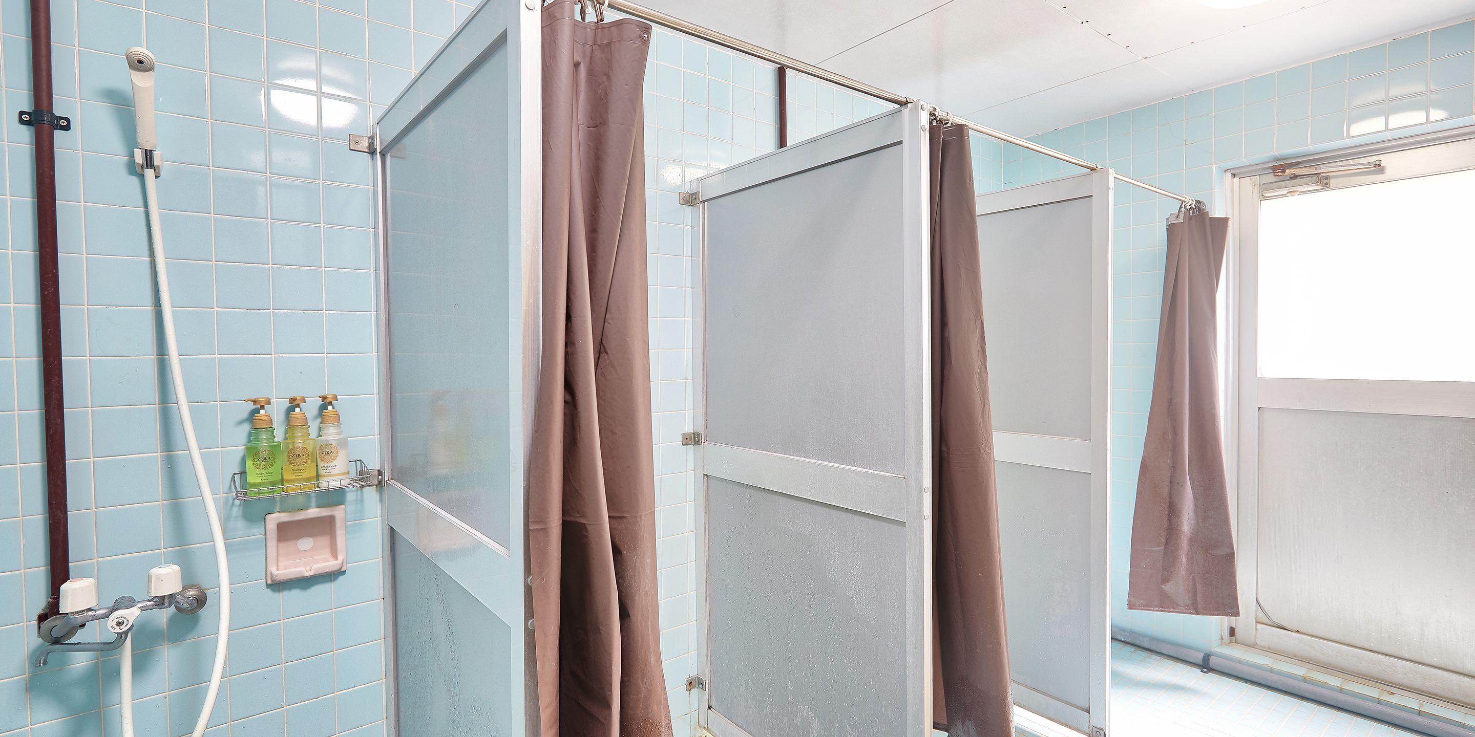 Une salle de bain avec un espace douche fermé, une fenêtre et une étagère contenant des articles de toilette.