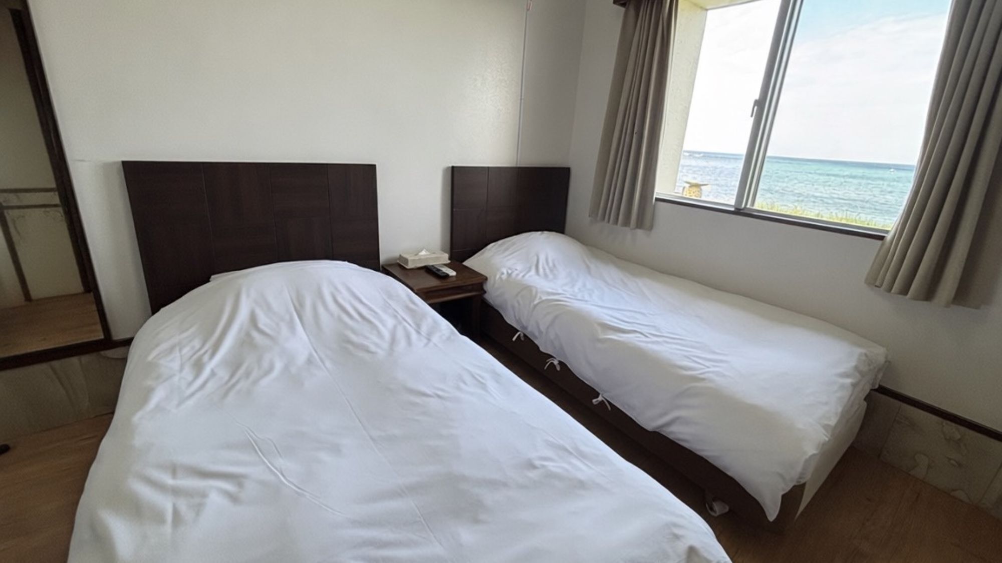 Een hotelkamer met twee eenpersoonsbedden, een nachtkastje, een afstandsbediening en een raam met uitzicht op zee.