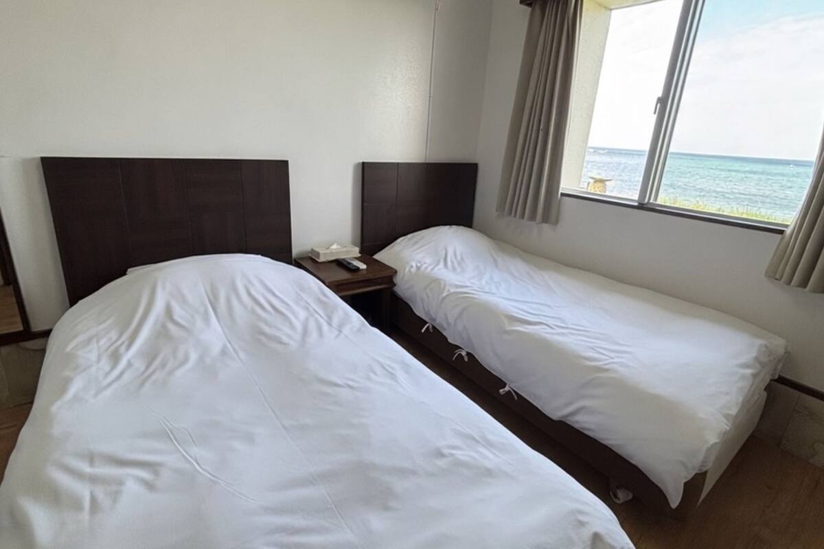 Een hotelkamer met twee eenpersoonsbedden, een nachtkastje, een afstandsbediening en een raam met uitzicht op zee.