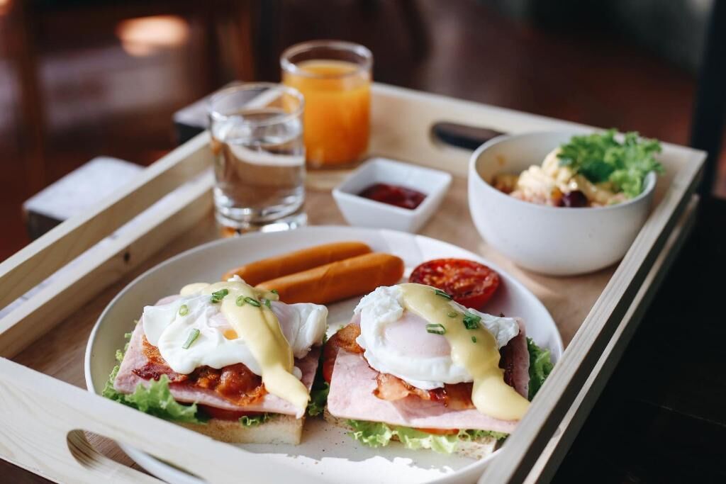 A tray with two poached eggs on toast, a small bowl of greens, a glass of orange juice, and a hot dog.