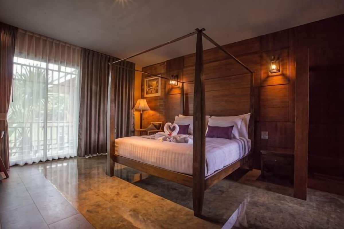 A four-poster bed with a canopy, a bedside table with a lamp, and a framed picture on the wall.