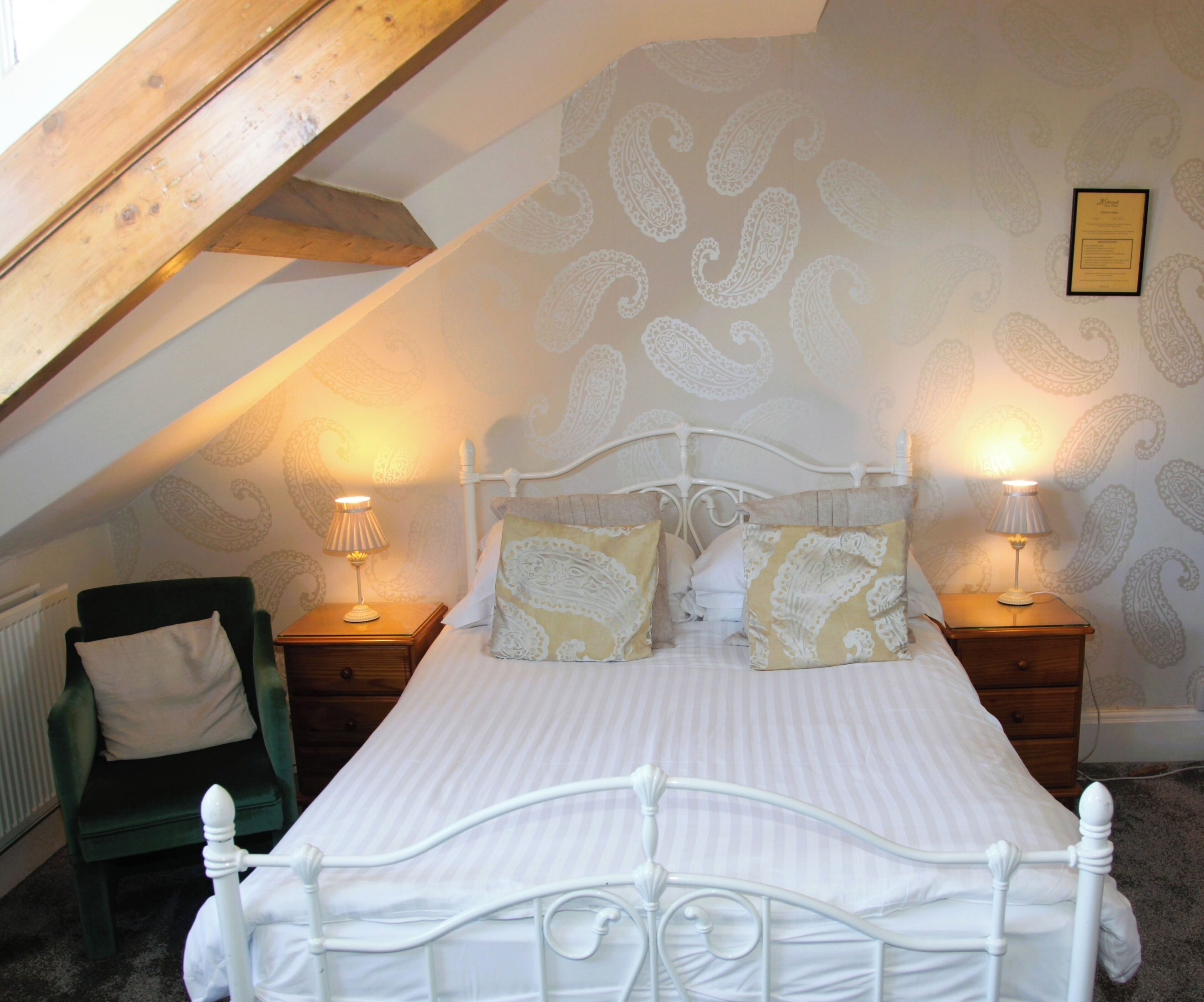 A bedroom with a sloped ceiling, a bed with white bedding and patterned pillows, two bedside tables with lamps, and a radiator.