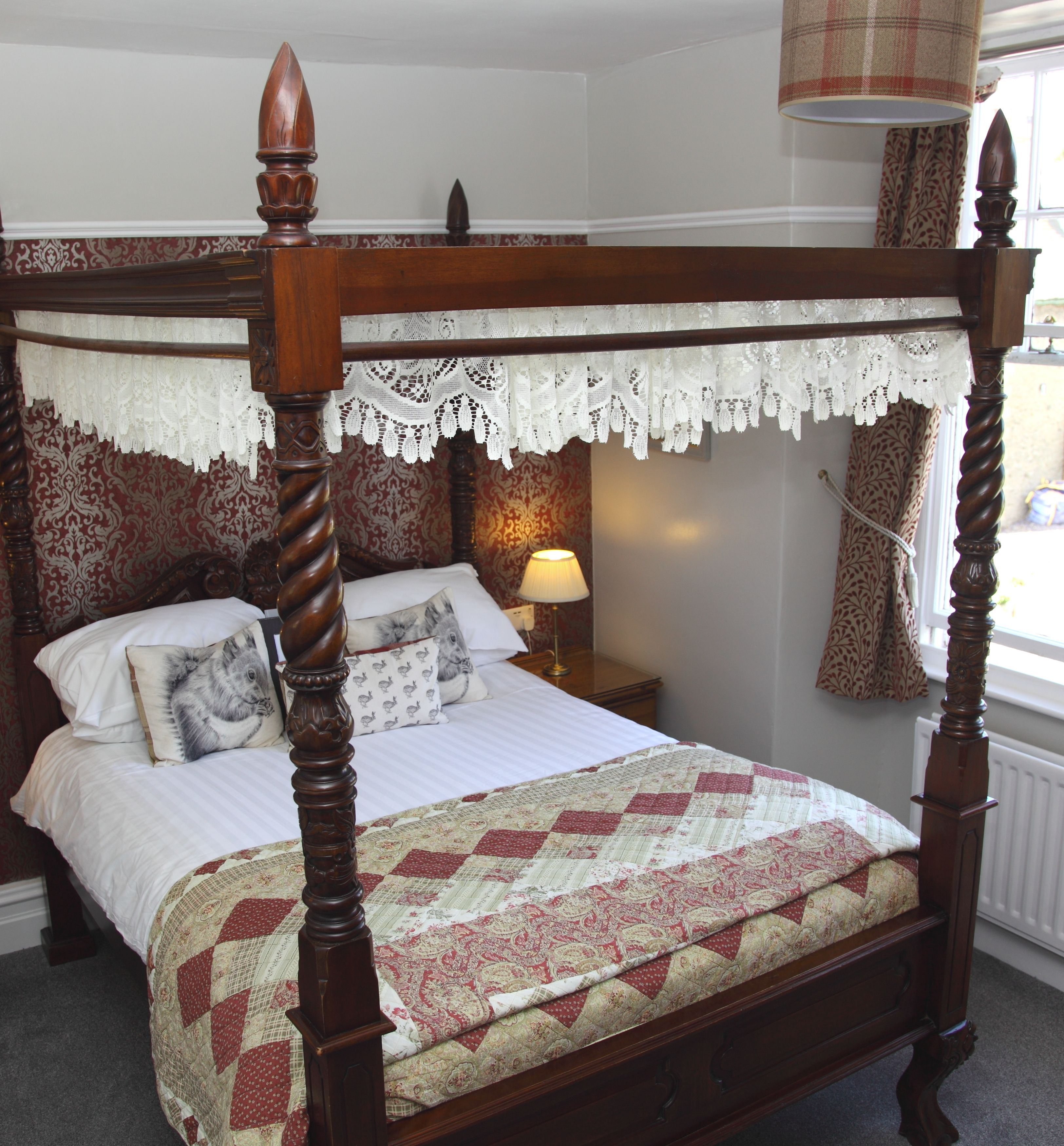 A four-poster bed with a lace canopy, a quilted bedspread, and patterned pillows.