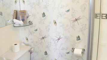 Un baño con inodoro, un estante de vidrio con artículos de aseo y una zona de ducha.