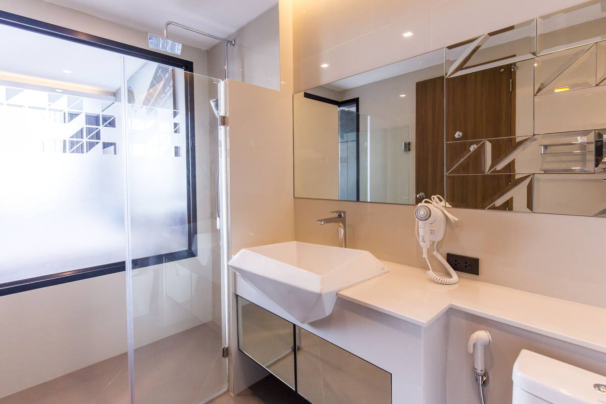 Une salle de bain moderne avec une douche à parois de verre, un lavabo blanc, un sèche-cheveux et des toilettes.