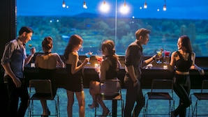 Un bar con vistas a un paisaje montañoso, sillas metálicas y luces colgantes.
