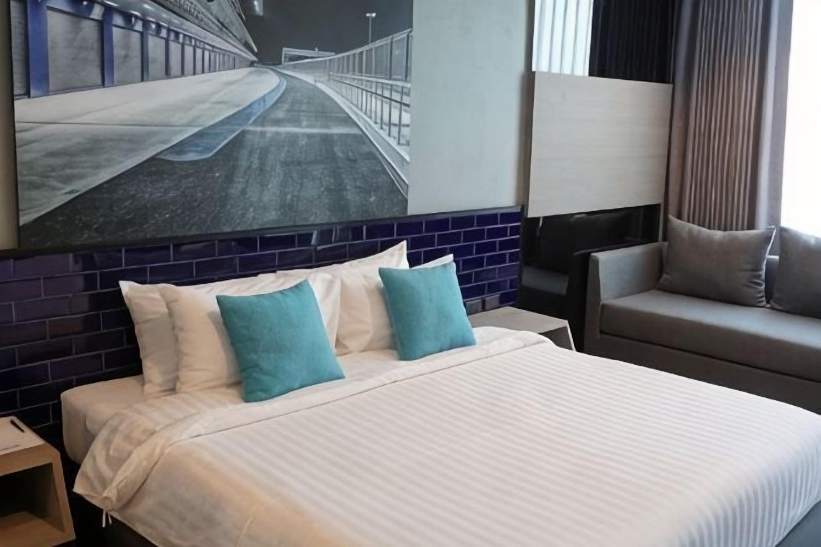 Een hotelkamer met een groot bed, een nachtkastje, een zithoek met een bank en een groot schilderij aan de muur.