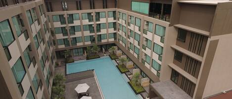 A modern building with multiple floors, a central courtyard with a swimming pool, and outdoor seating areas.