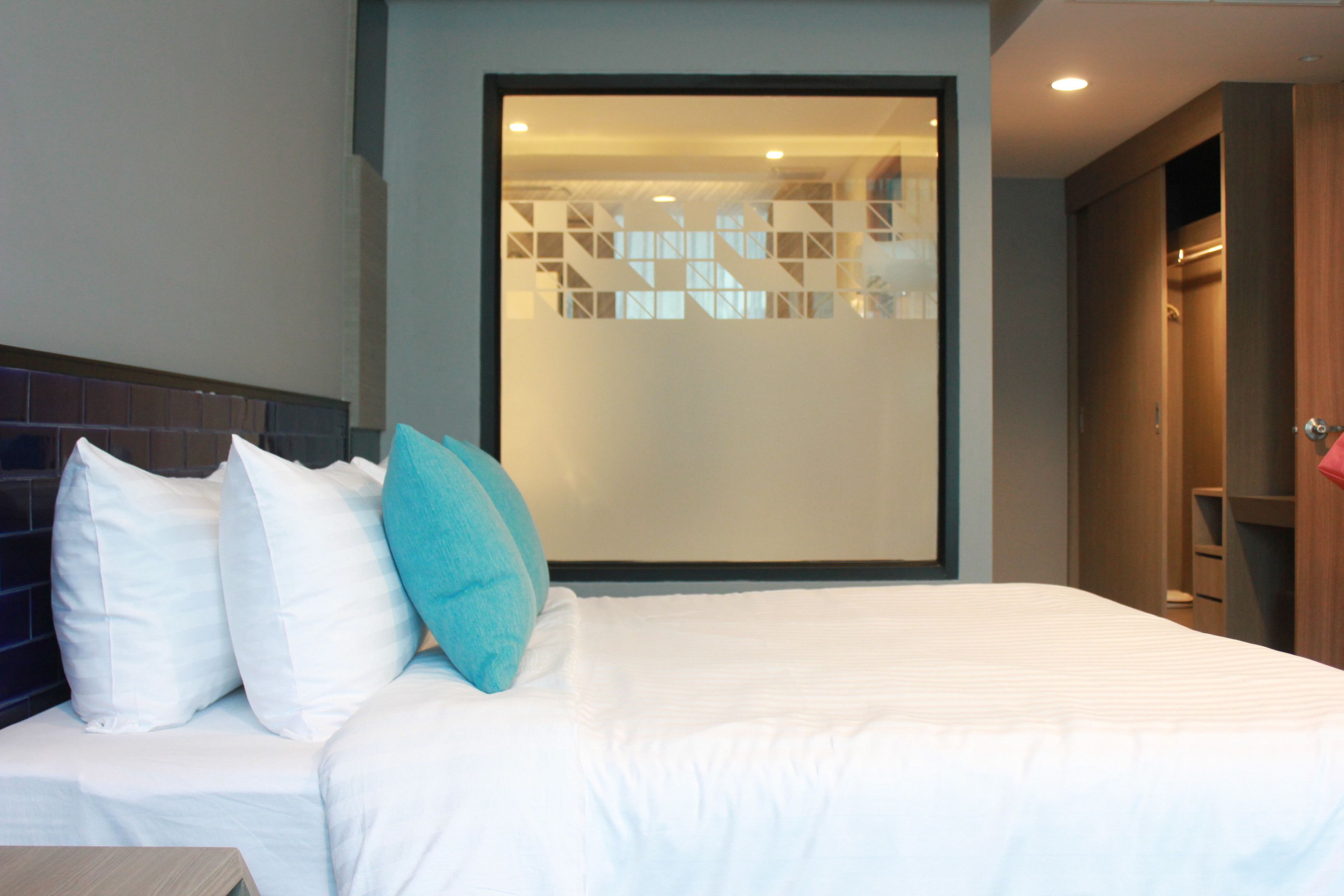A modern hotel room with a large bed, a view through a frosted glass partition, and a wooden wardrobe.