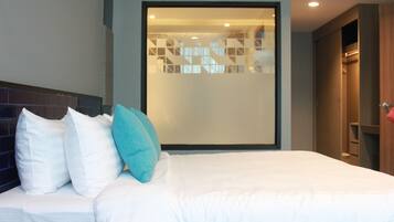 A modern hotel room with a large bed, a view through a frosted glass partition, and a wooden wardrobe.