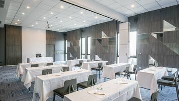 Sala de conferência com mesas organizadas para reuniões, equipada com cadeiras e mesas, e um design moderno no teto.