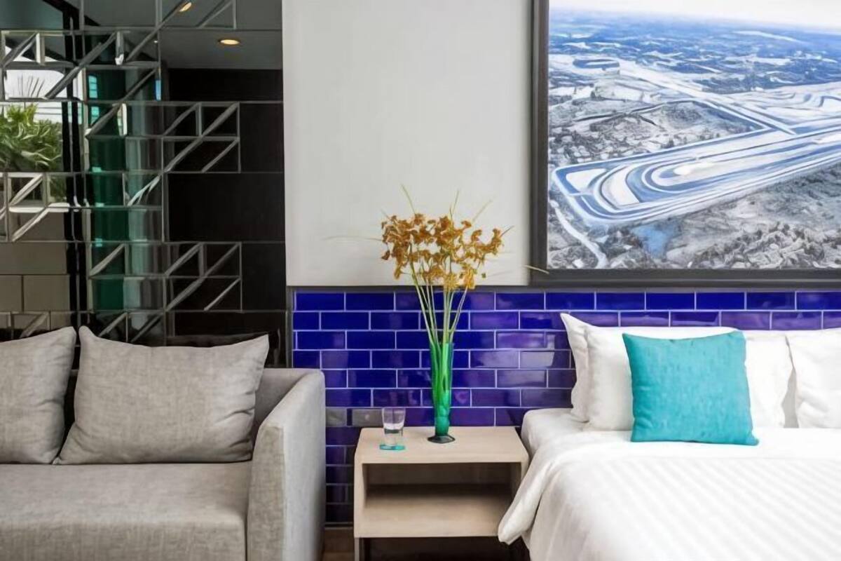 Une chambre d’hôtel avec un lit, une table de chevet, un vase de fleurs, une fenêtre donnant sur le paysage urbain et un escalier.