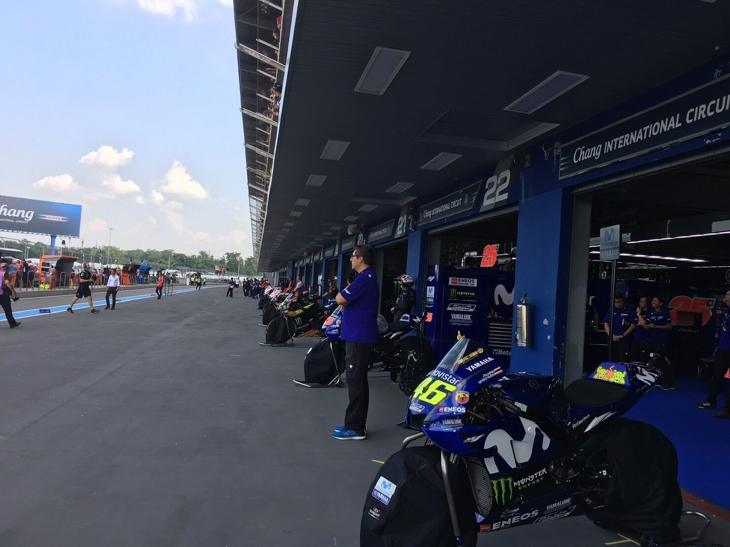 A motorcycle parked in a garage with a blue and white color scheme, a sign reading "Chang International Circuit", and a person standing nearby.