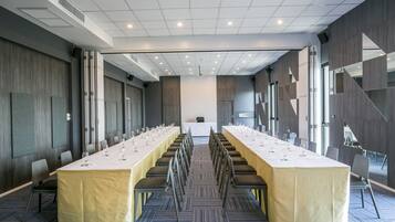Una sala conferenze con un lungo tavolo, sedie e una tovaglia bianca.