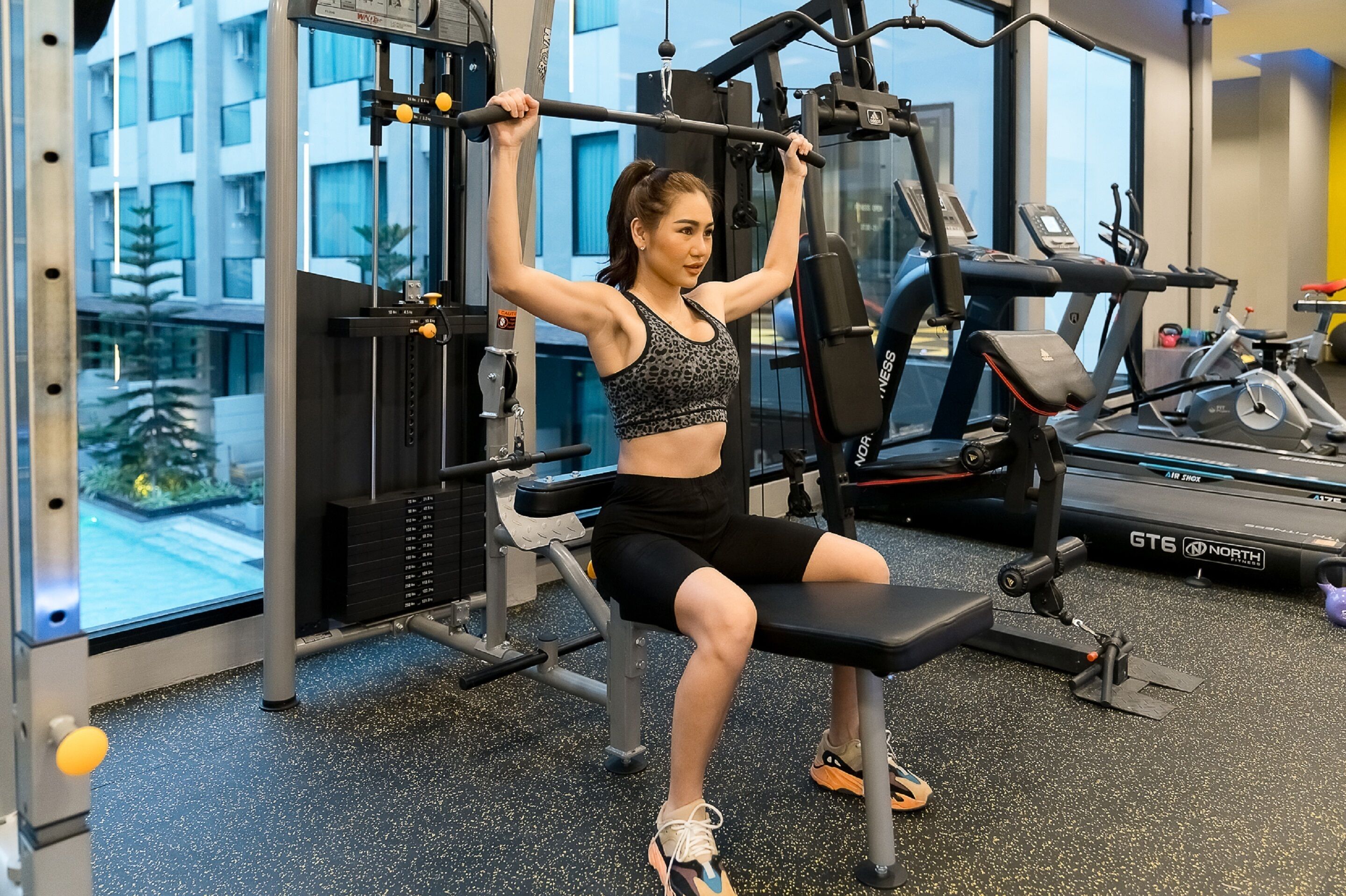 A gym with exercise equipment, a treadmill, and a view of a building outside.