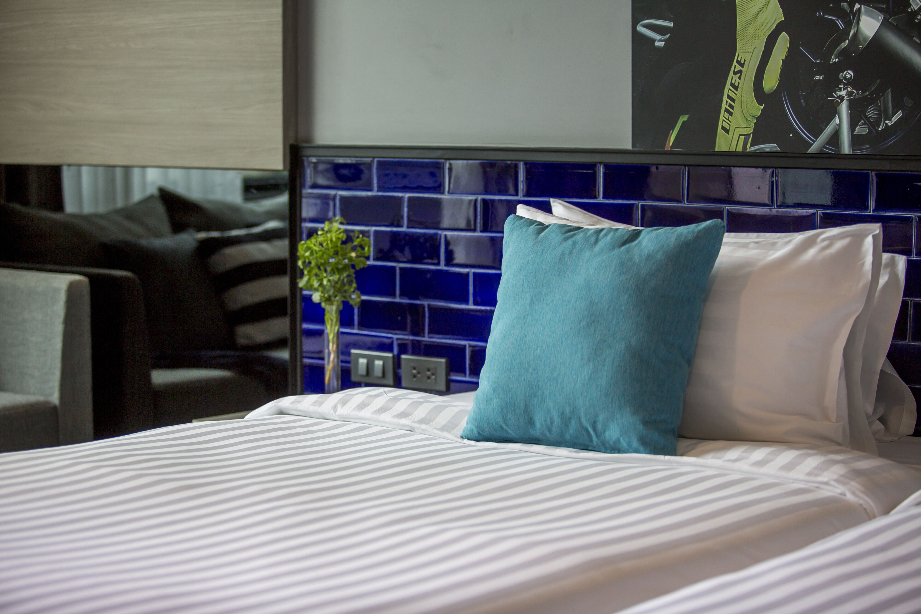 Habitación de hotel con cama, cabecera de azulejos azules y blancos, una planta pequeña y una almohada.
