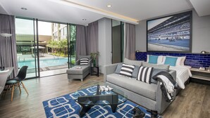 Habitación de hotel moderna con puerta corredera de vidrio que da a una piscina, un sofá gris con cojines a rayas, una mesa de centro de vidrio y un cuadro grande enmarcado con una imagen de una carrera.