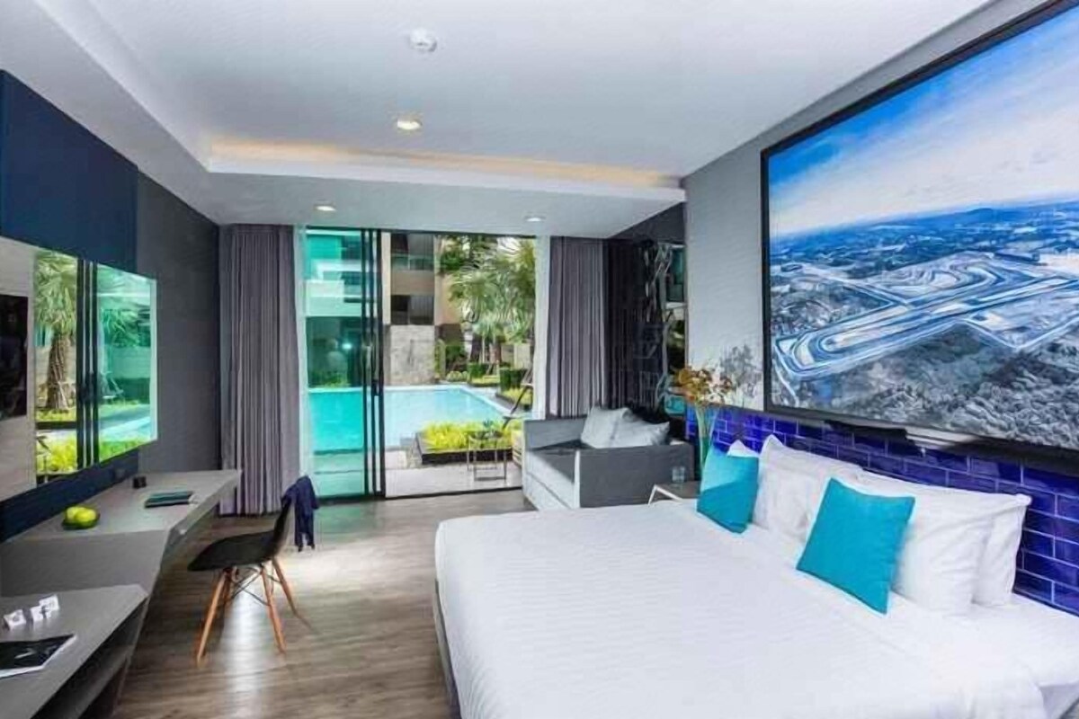 A modern hotel room with a large bed, a TV, a desk, and a view of a swimming pool.