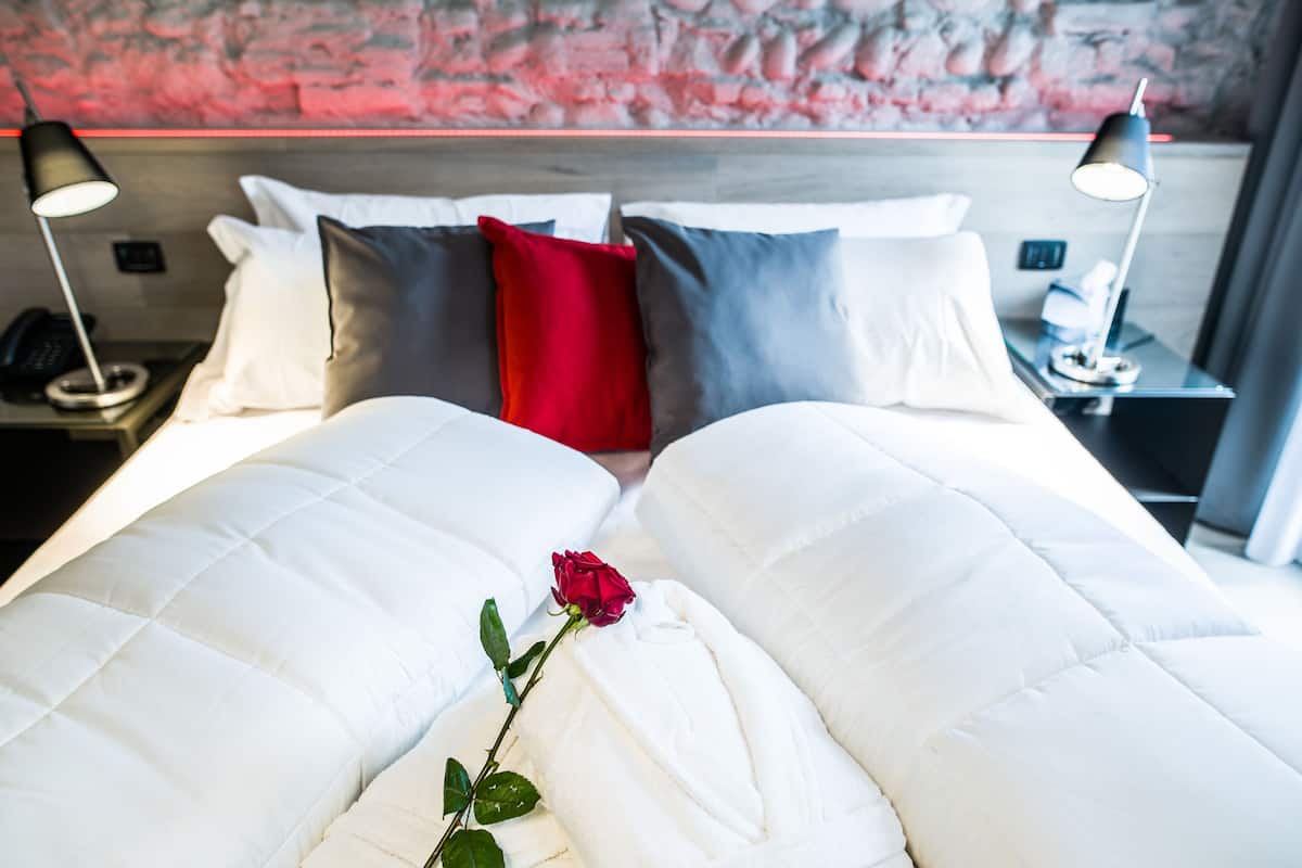 A hotel room with a large bed, white bedding, a red rose, and two bedside lamps.