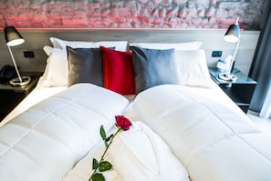 Ein Hotelzimmer mit einem großen Bett, weißer Bettwäsche, einer roten Rose und zwei Nachttischlampen.