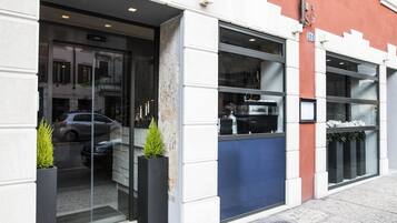 Ingresso di un edificio con porte in vetro, un'auto parcheggiata e piante in vaso.