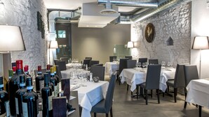 A restaurant with tables set for dining, wine bottles on display, and a stone wall. - Locanda al Vescovo (Verona)