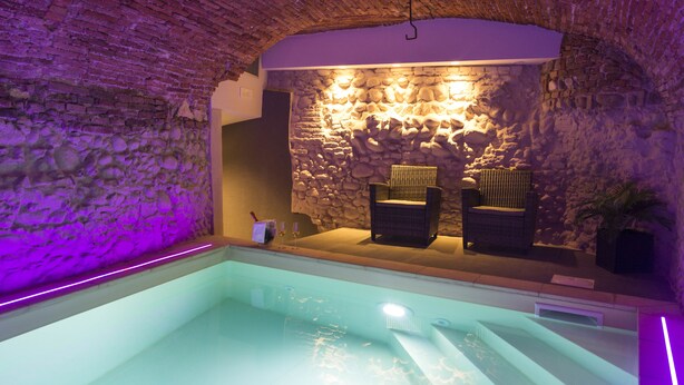 A spa area with a stone wall, two wicker chairs, and a pool. - Locanda al Vescovo (Verona)
