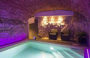 Ein Wellnessbereich mit einer Steinwand, zwei Korbstühlen und einem Pool.