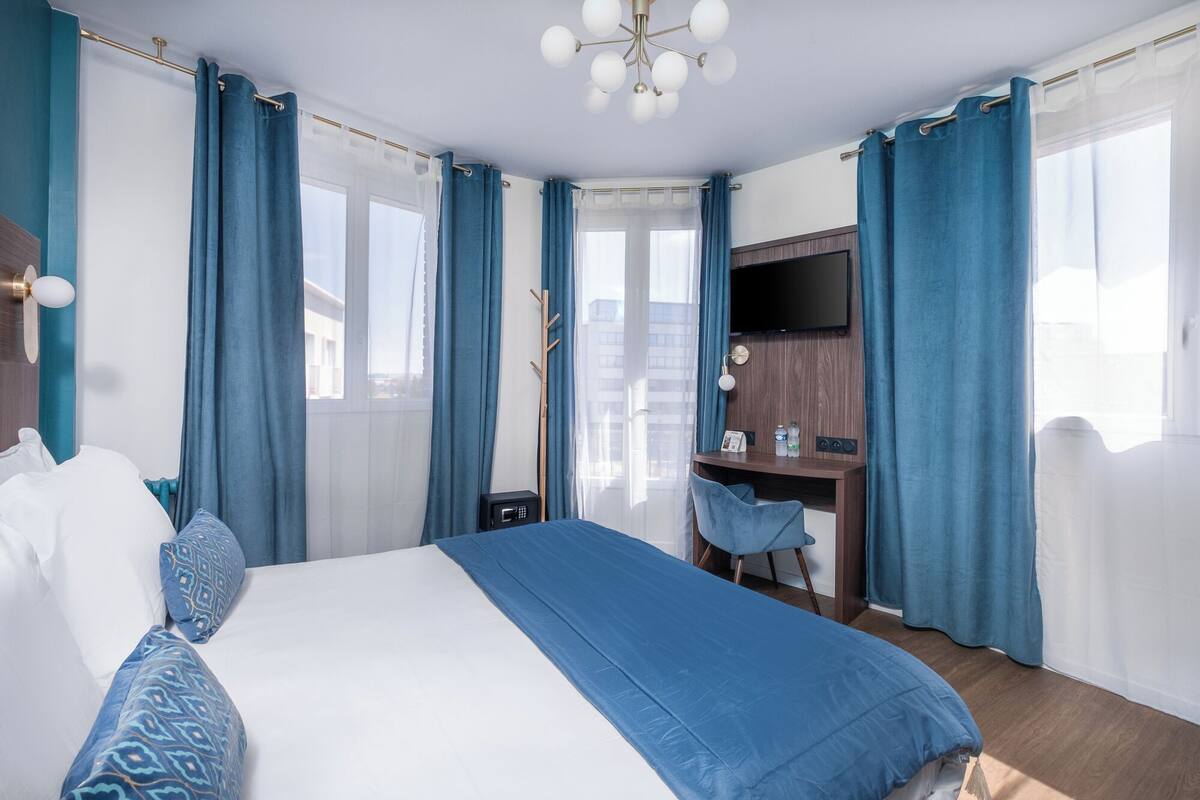 A hotel room with a large bed, a desk, a chair, a TV, and a window with curtains.