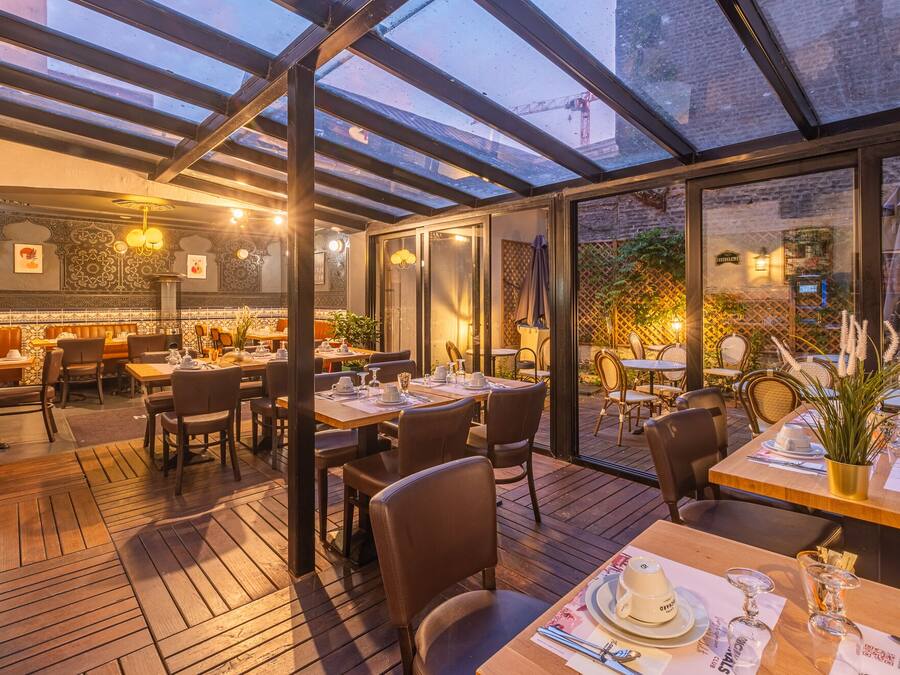 Un comedor con espacio interior y exterior, suelo de madera, mesas dispuestas para comer y techo de vidrio.