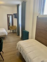 A hotel room with two single beds, a wooden floor, a radiator, a chair, and a large mirror.