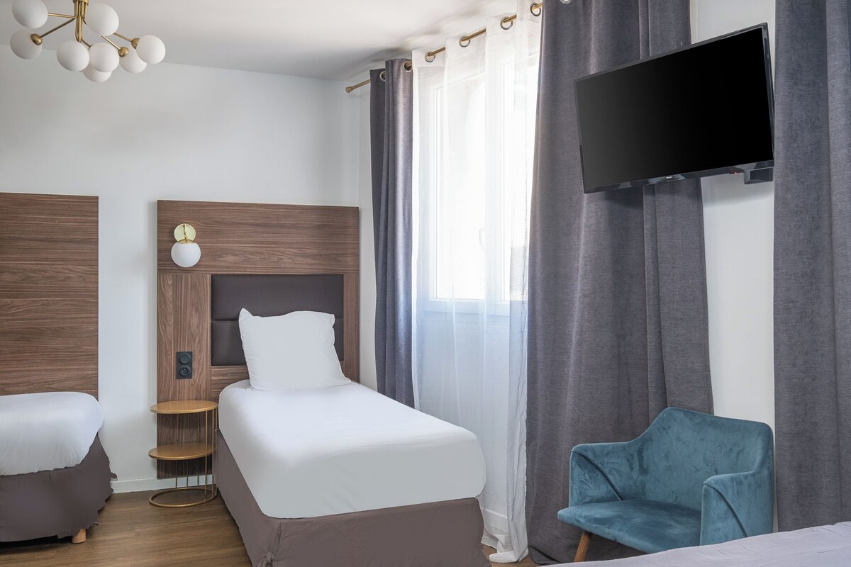 Una habitación de hotel moderna con una cama, televisor, una silla y un cabecero de madera.