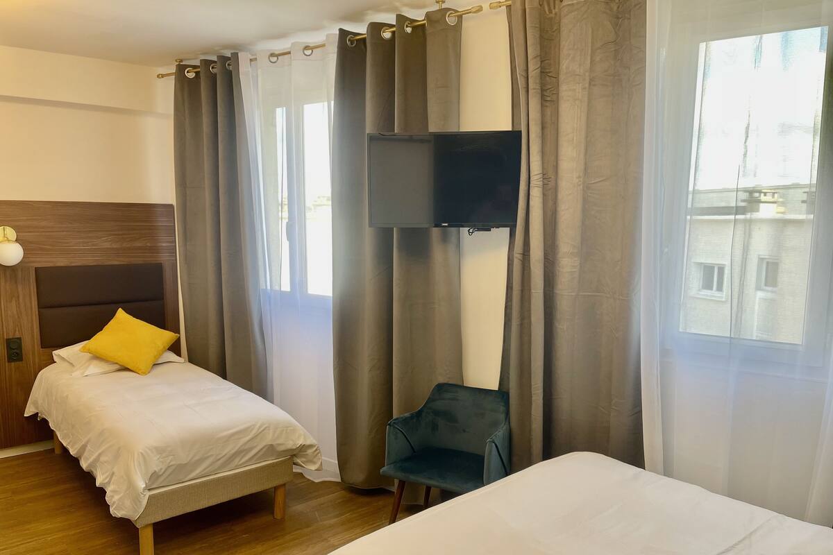 A hotel room with two beds, a TV mounted on the wall, a chair, and a window with curtains.