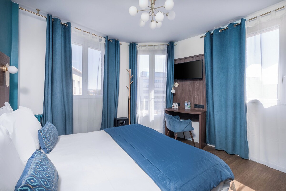 A hotel room with a large bed, a desk, a chair, a TV, and a window with curtains.