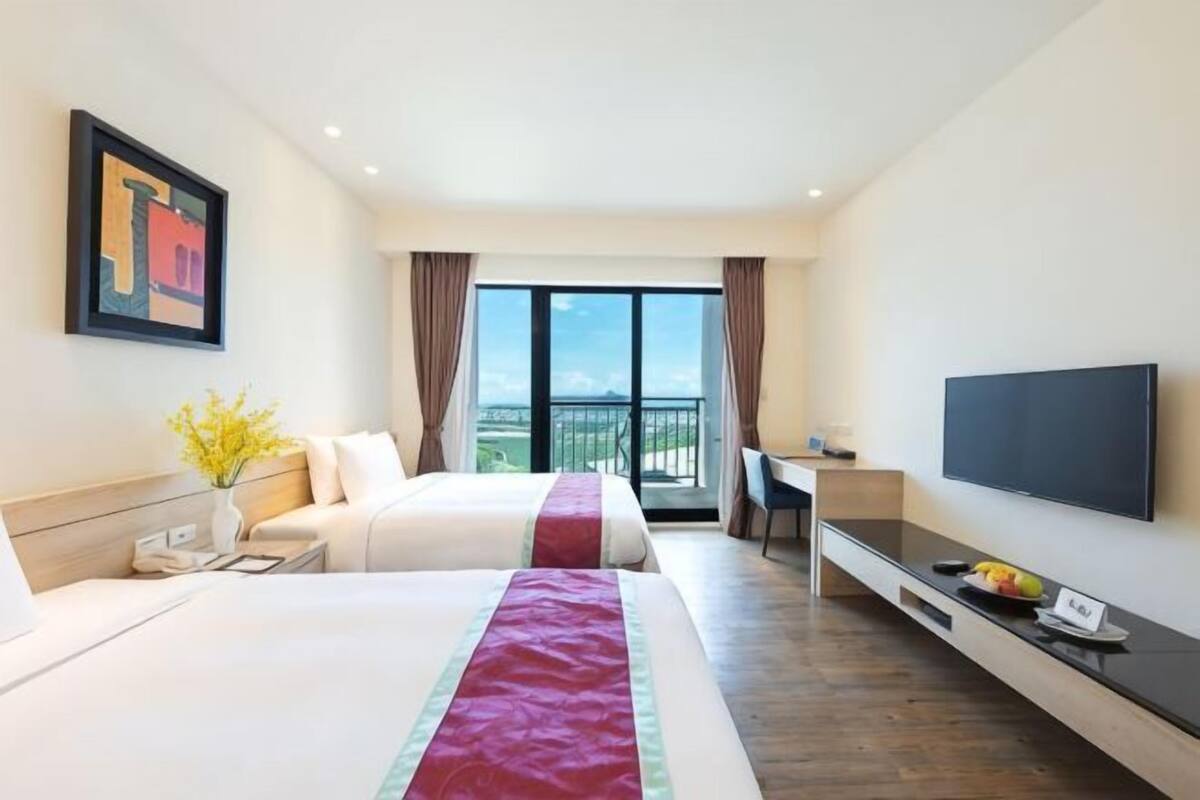 A hotel room with two beds, a TV, a desk, and a balcony with a view.