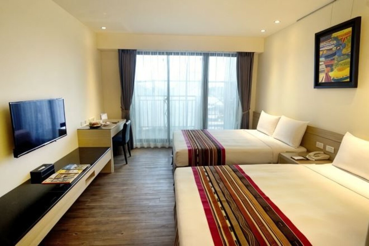 Habitación de hotel con dos camas, televisión, escritorio y ventana con cortinas.