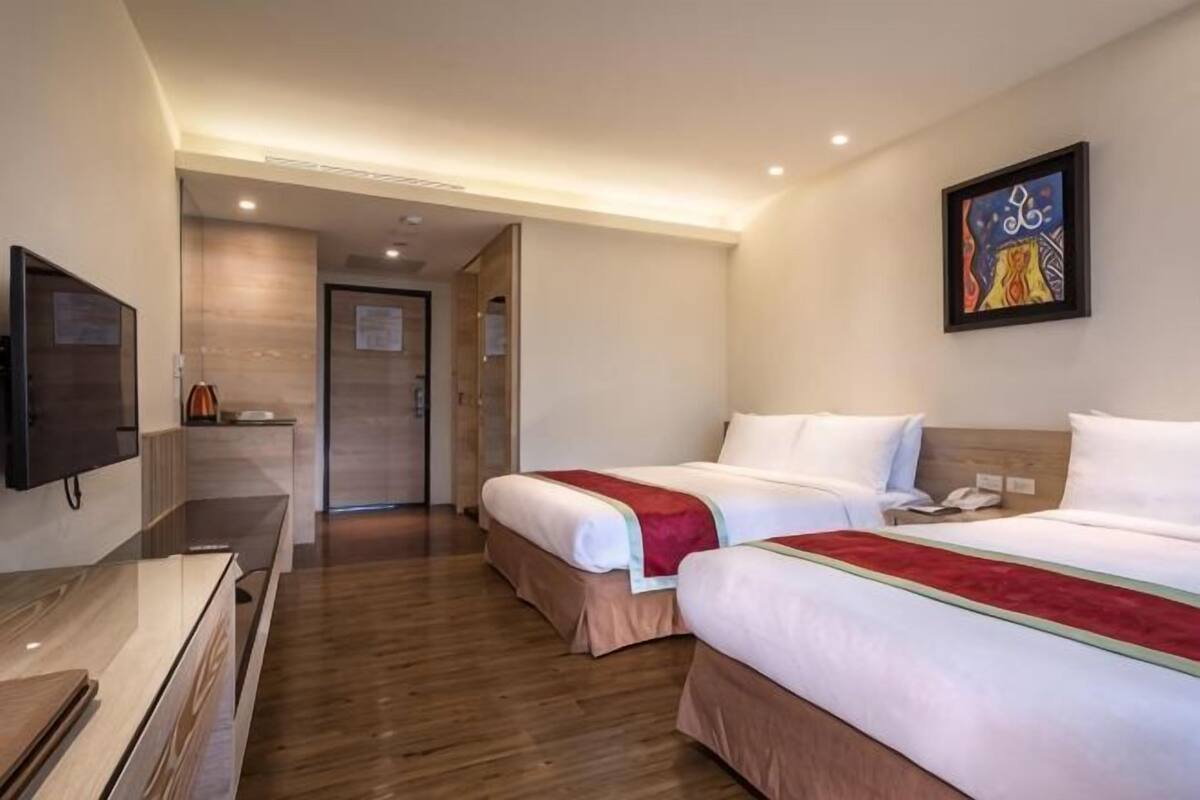 A hotel room with two beds, a TV, a desk, and a painting on the wall.