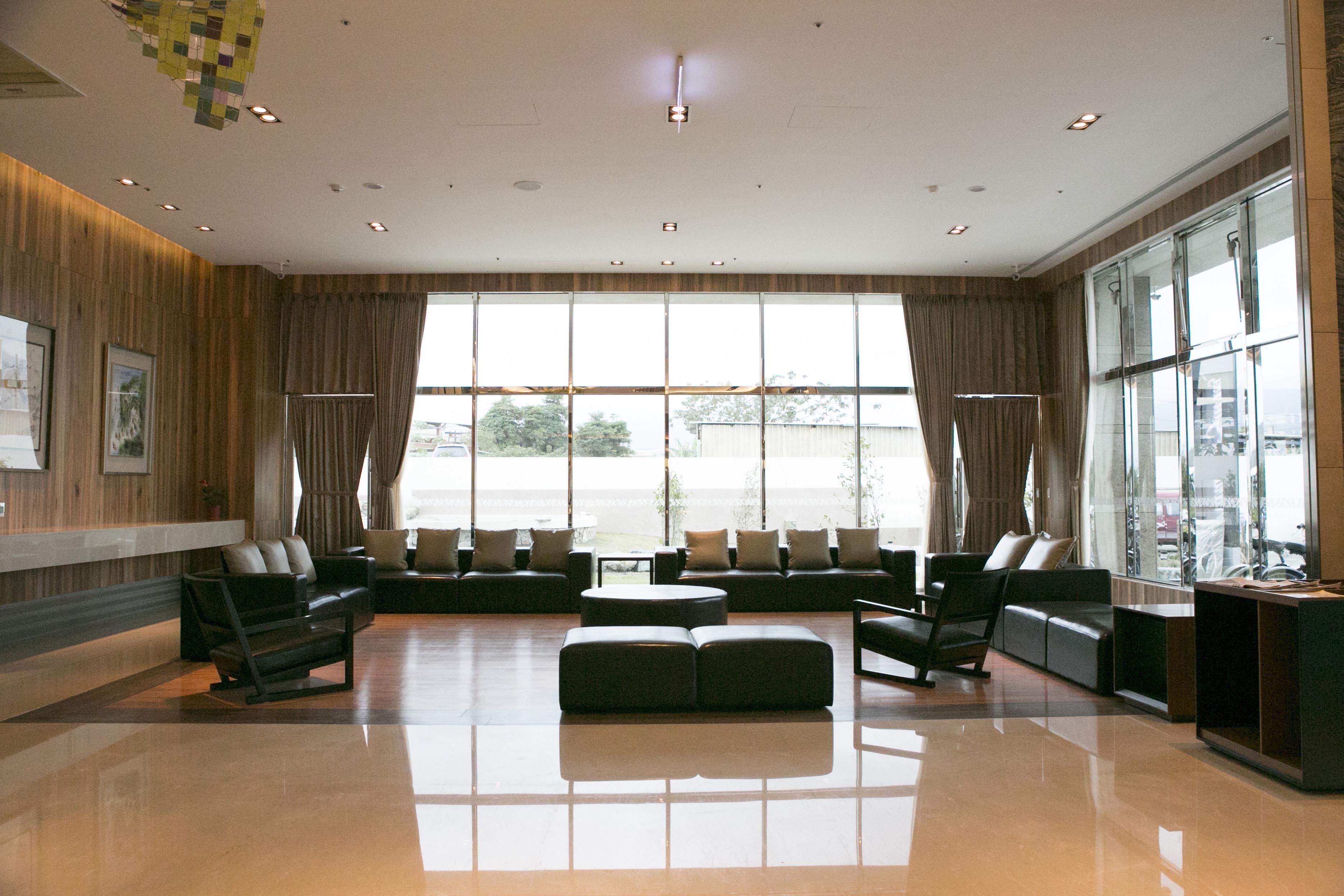 A spacious lobby with a large seating area, a reception desk, and large windows providing a view of the outdoors.