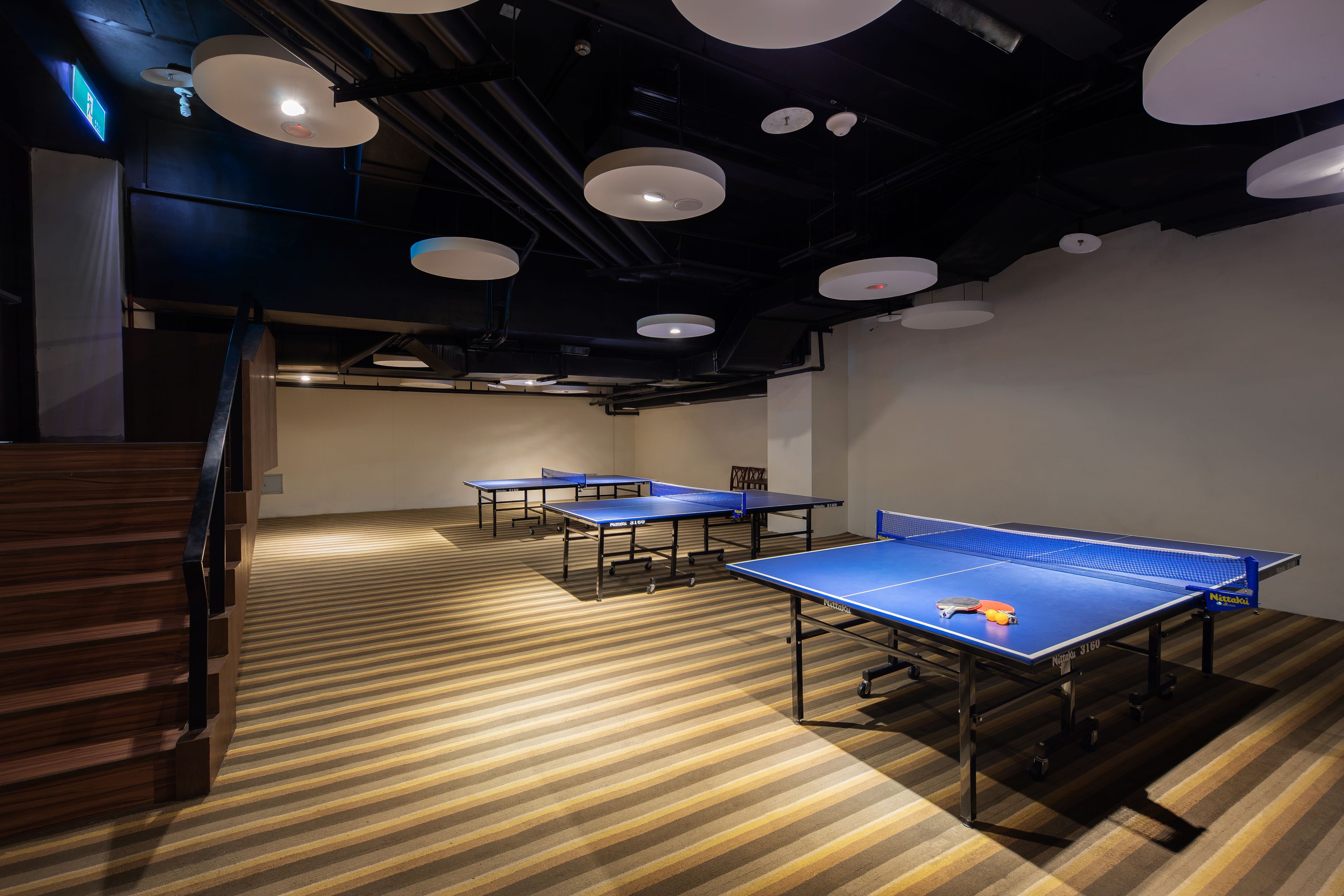 Una habitación con mesas de ping pong, una escalera y luminarias modernas.