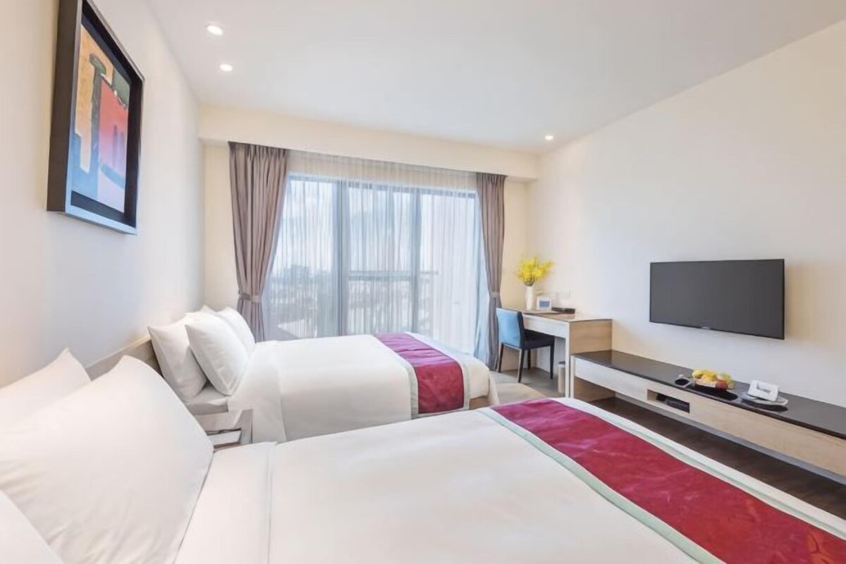 Habitación de hotel con dos camas, un escritorio, un televisor y un ventanal grande.
